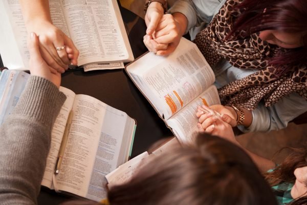A group of young women bow their heads and pray with bibles.