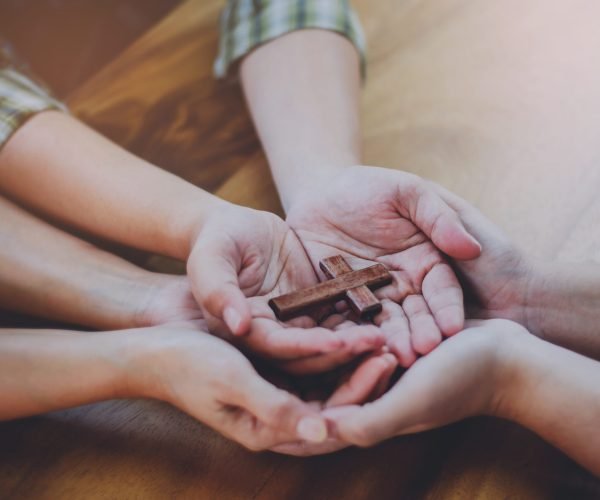 Three people hands holding small wooden cross on wood table, Christian concept Jesus is the center of life or ministry , copy space.